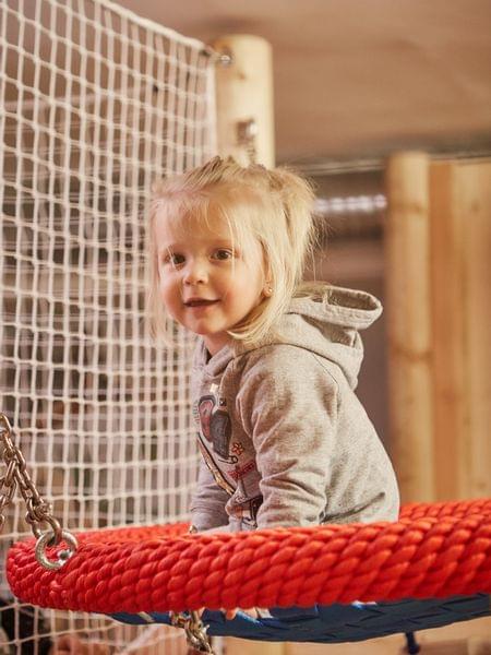 Indoor action / indoor fun Little girl on a red rope swing in an indoor playground
